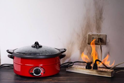 A slow cooker plugged into an extension cord that has caught fire.