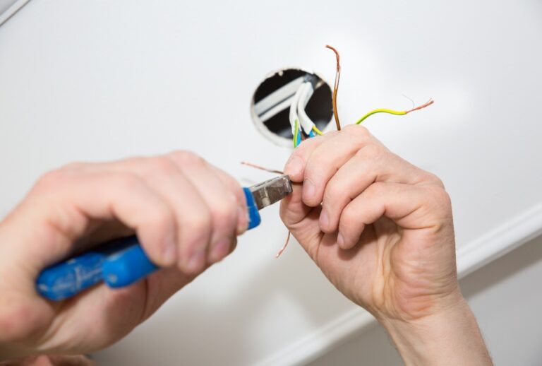 An electrician is working on a rewiring project in a home. He is holding plyers to repair the wires.