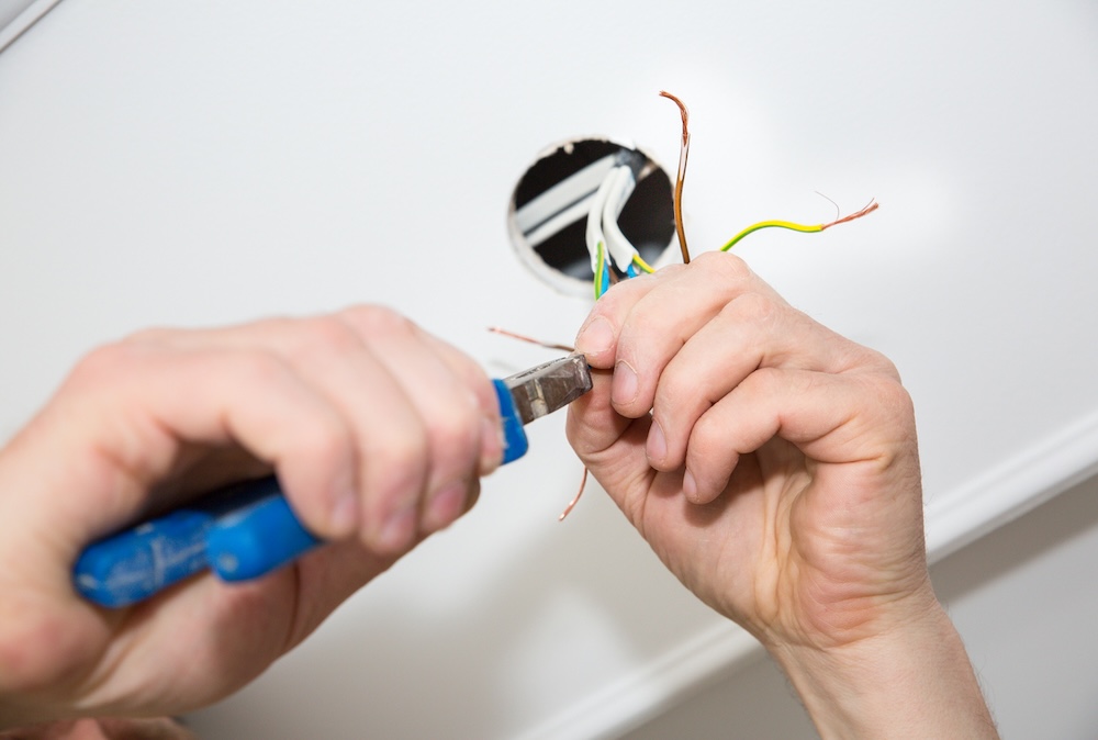 An electrician is working on a rewiring project in a home. He is holding plyers to repair the wires.