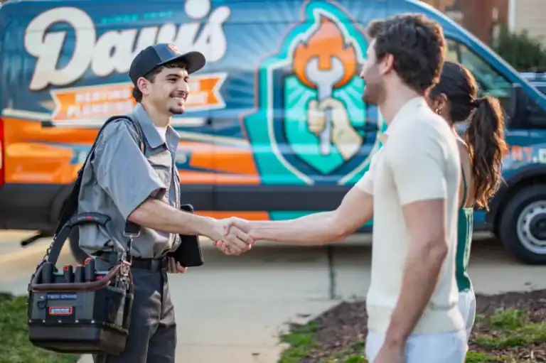 A technician in uniform, demonstrating excellent customer service, shakes hands with a man outside, while a woman stands nearby. A colorful service van is parked in the background.